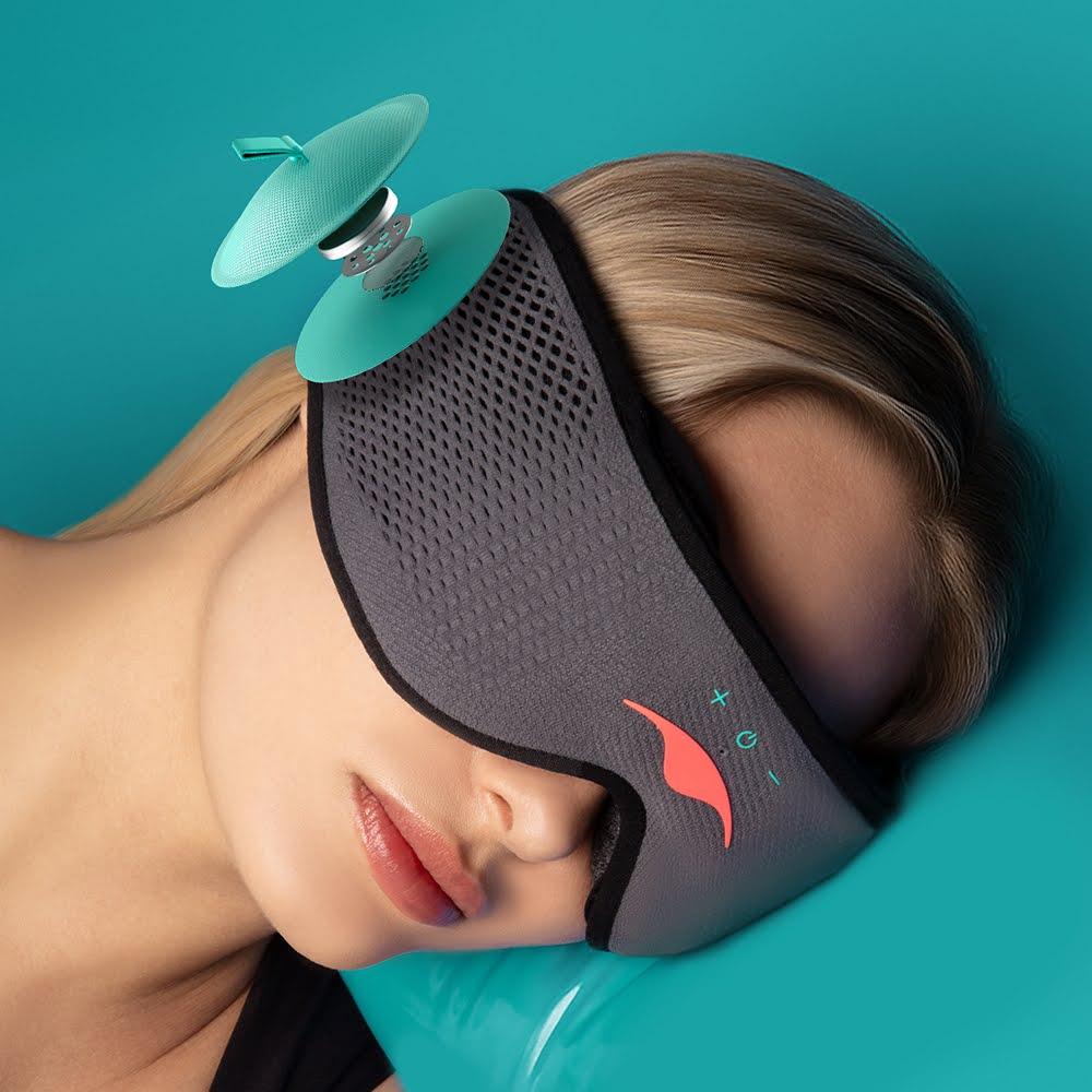 A blonde girl lying down with her head to the side, wearing a gray Bluetooth® sleep mask. A blue speaker is seen coming out from the side of the mask.