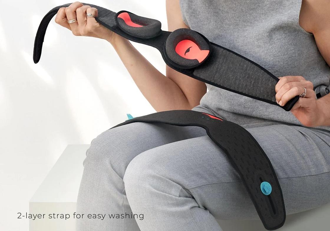 A person shown from chest up holding the inner layer of a black mesh Bluetooth sleep mask with C-shaped eye cups. The outer layer of the sleep mask is on the person's lap facing upward.