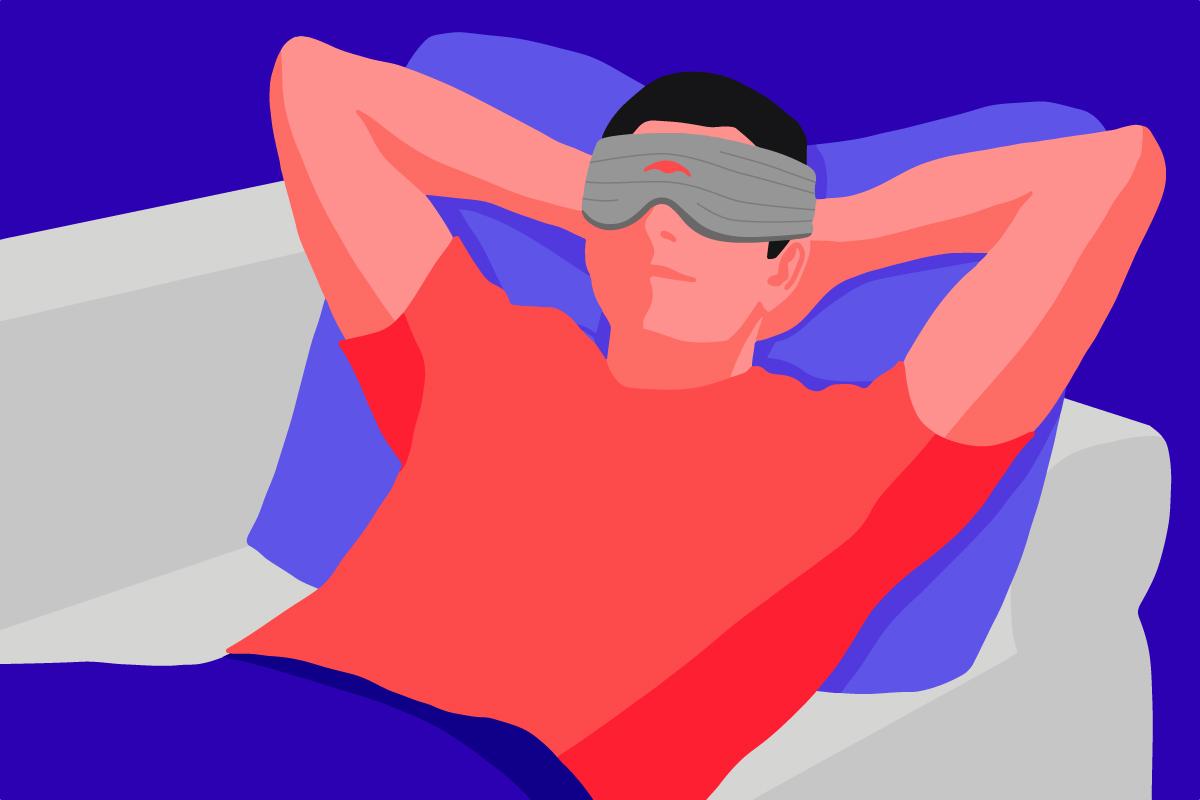 A man relaxing on a couch wearing a gray pressure eye mask with eye cups.