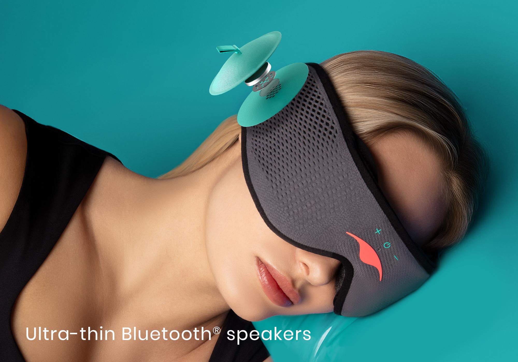 A girl lying down on her side, wearing a gray mesh Bluetooth sleep mask with a circular speaker on the side of the mask.