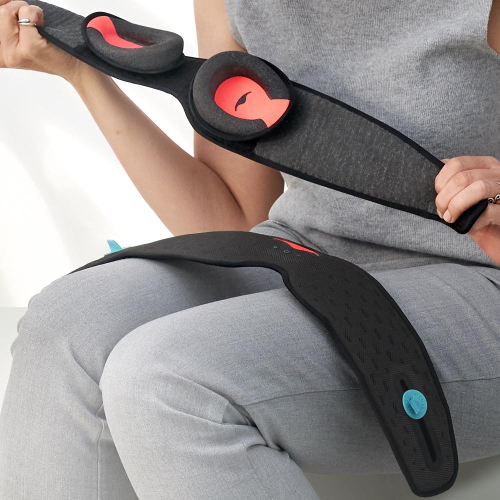 A person holding the inner strap of a sleep mask with built-in speakers and detachable eye cups. The outer strap is draped across the person’s thighs.