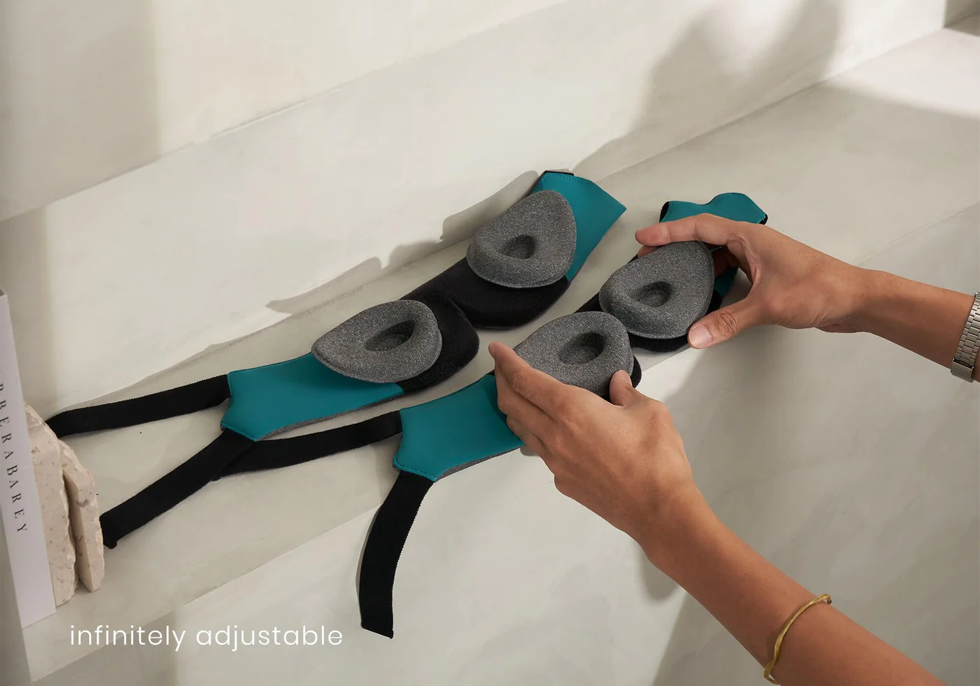 Two weighted sleep masks for side sleepers laid out flat, interior facing upward. Each mask has a pair of gray eye cups. Hands are demonstrating how the cups can be adjusted.